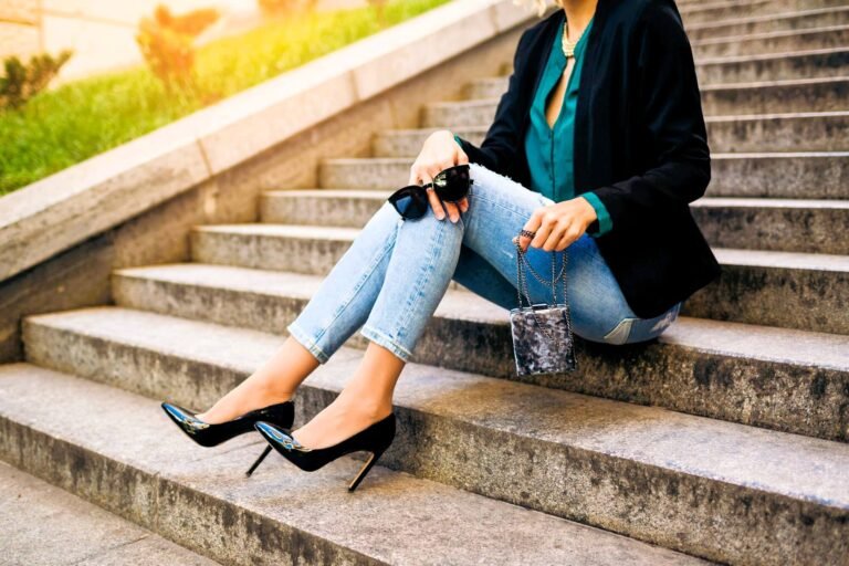 woman wearing high heels, jeans, black jacket sitting on stairs in town